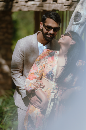 A romantic couple shares an intimate outdoor moment, with one wearing a light gray suit and the other in a floral dress.