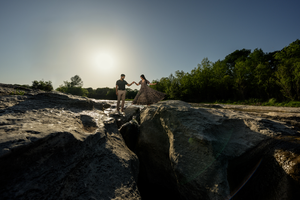 Candid silhouettes from a couple shoot in rocky terrain at sunset with trees in the background on a summer evening.