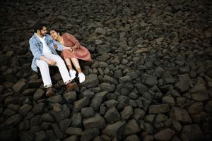 A couple sits together romantically on a black rocky beach surface under dramatic lighting.