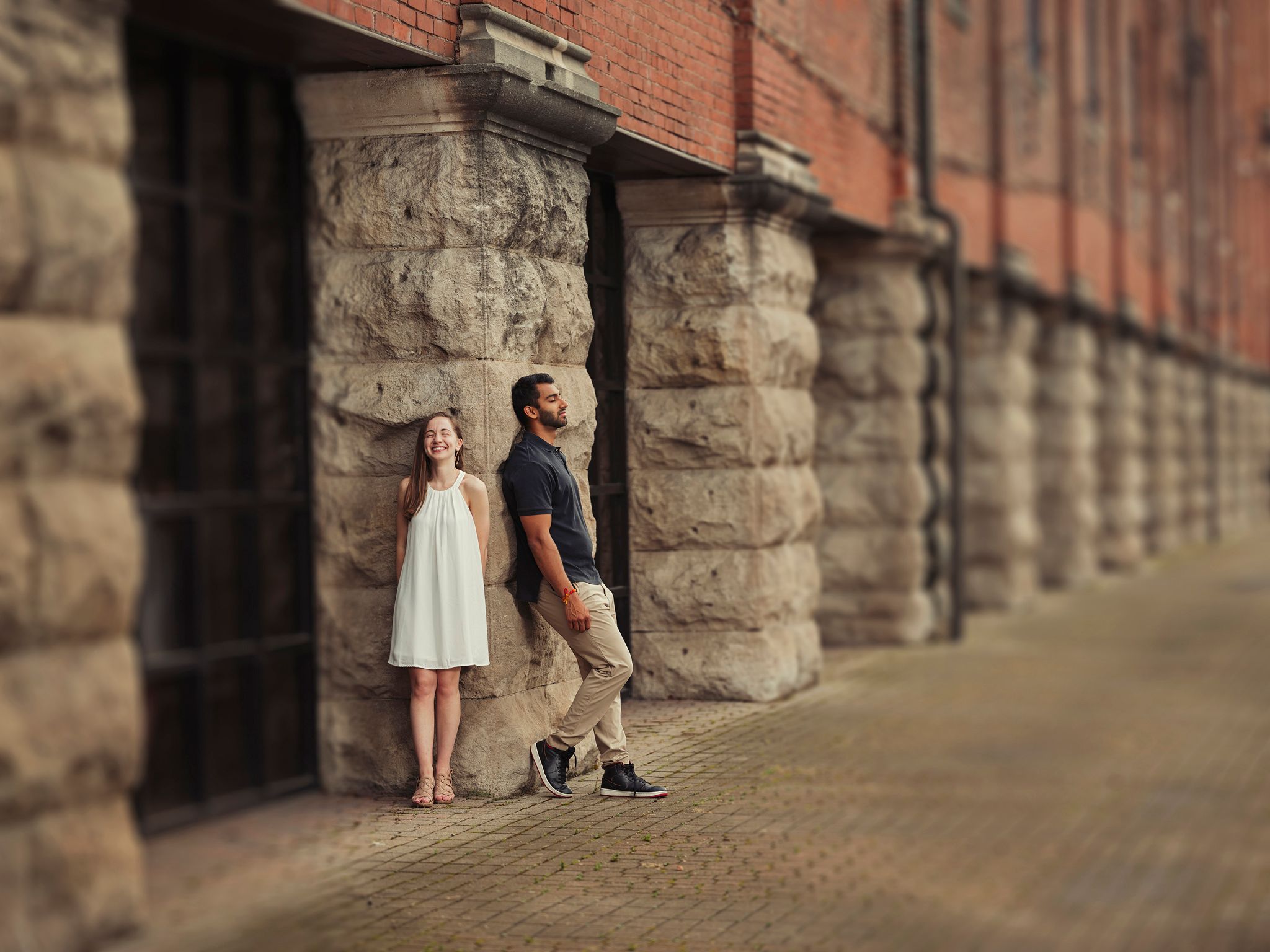 Two people stand against a rustic stone and brick wall in an urban setting during golden hour.