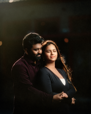 An indian couple shares an intimate moment in moody low-key lighting creating a romantic silhouette effect.