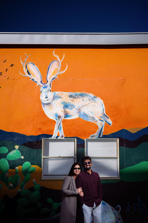 Newly wedded Bride and Groom stand in front of a vibrant orange wall mural featuring a large white rabbit.