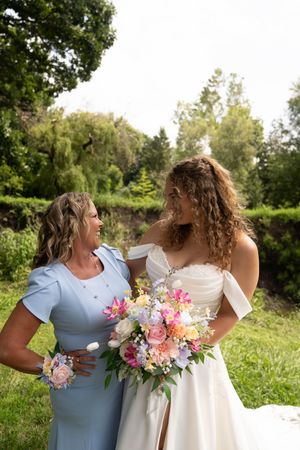 Bridesmaids in light blue dresses hold vibrant pink and white bouquets in an outdoor garden setting.