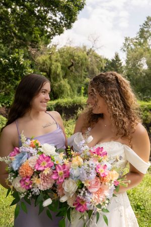 Wedding party holding beautiful multicolored bouquets of pink, white, and purple flowers outdoors.