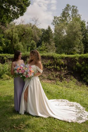 Wedding dress with long lace train photographed in a sunny meadow with green trees in background.