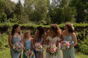 Bridal party in soft blue dresses share candid moments while holding vibrant floral bouquets.