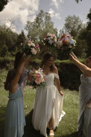 Bridesmaids in light blue dresses pose with floral bouquets in a sunny outdoor setting.