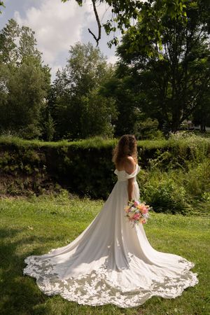 White wedding dress with intricate lace train spreads across green grass in outdoor garden setting.