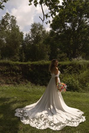 A flowing white wedding dress train spreads elegantly across green grass in a garden setting.