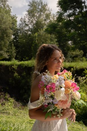 Vibrant pink and peach bridal bouquet held in a sunny outdoor garden setting.