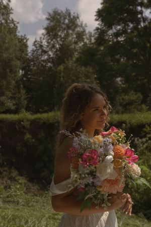 A bride holds a vibrant bouquet of pink and white flowers in an outdoor garden setting.