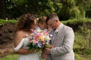 Romantic wedding portrait with colorful floral bouquet against a natural outdoor backdrop.