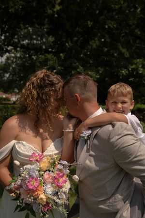 Intimate wedding moment captured with vibrant pink and peach bouquet in an outdoor setting.