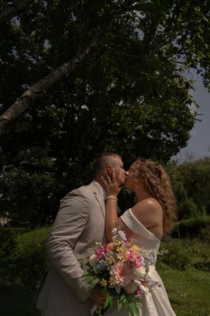 Romantic wedding portrait with colorful summer bouquet in a sunlit garden setting.