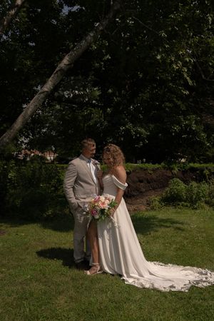 Elegant wedding couple poses on manicured lawn with flowing white dress train.