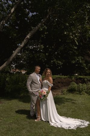 Wedding couple poses in a garden setting with flowing white dress and light gray suit.