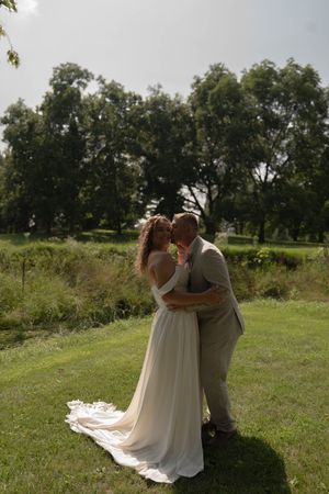 Wedding couple shares an intimate moment on sunny grass field with dramatic dress train.