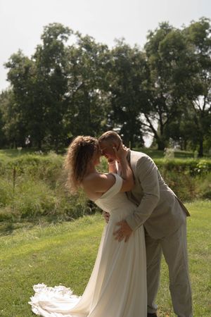 A romantic wedding couple shares an intimate moment outdoors with trees in the background.