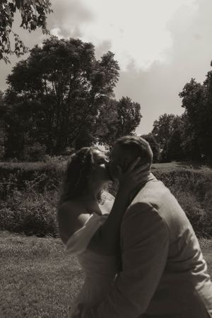 A black and white wedding photo captures a tender moment between newlyweds in a natural setting.