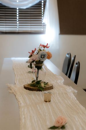 A delicate floral centerpiece sits on a wooden slice with white table runner decor.