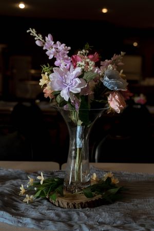 An elegant floral arrangement with pink and white flowers in a glass vase on a rustic wooden base.