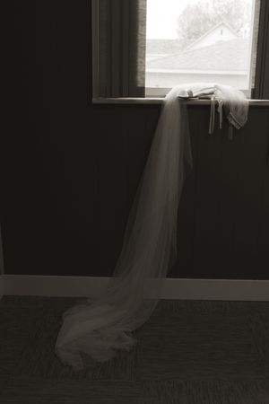 Silhouette of a bride's veil flowing dramatically in dark room with window light.