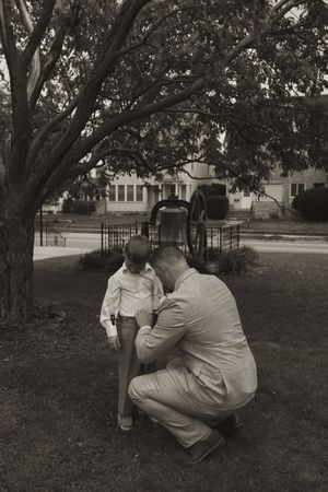 Wedding party members sharing intimate moments on a grassy lawn under large trees.