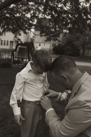 A tender moment during wedding preparations as a boutonniere is pinned onto formal attire outdoors.