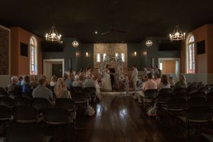 Dark reception hall with chandeliers and tables set for wedding celebration.