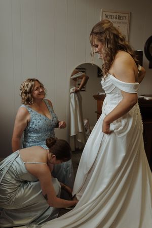Bridesmaids in blue dresses helping with wedding dress preparations.