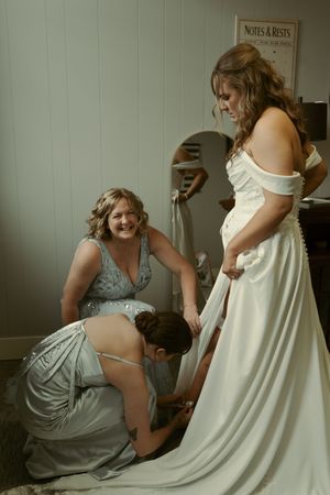 Bridesmaids in silver dresses assisting with the bride's wedding gown.
