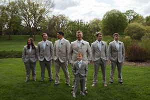 Wedding party members in gray suits and light blue attire stand in line on green grass.