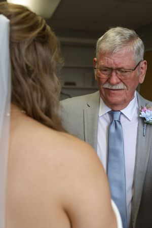 Emotional first look moment between a bride and an older gentleman in a light blue tie and glasses.