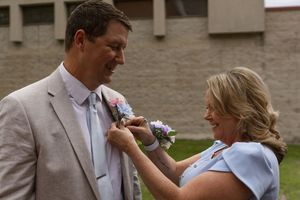 A boutonniere being pinned on a light colored suit jacket outdoors.