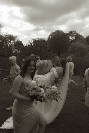 Wedding party poses in field under dramatic cloudy sky with flowing white dress and bouquets.