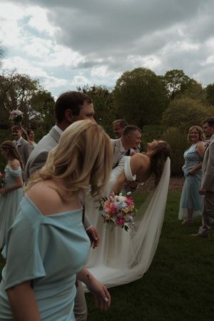 Wedding group celebrates joyfully in an outdoor garden setting with light blue bridesmaid dresses.