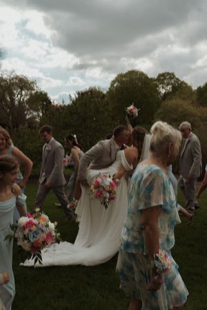 Wedding party poses together outdoors under cloudy skies with bridesmaids in blue dresses and colorful bouquets.