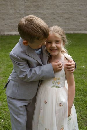 Two young wedding attendants share a sweet moment outdoors in formal attire.