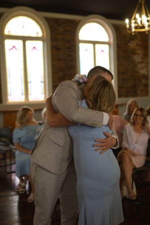 An emotional embrace during a wedding ceremony in a church with arched windows.