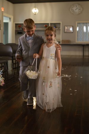 Young wedding attendants walking together on hardwood floors with scattered petals.