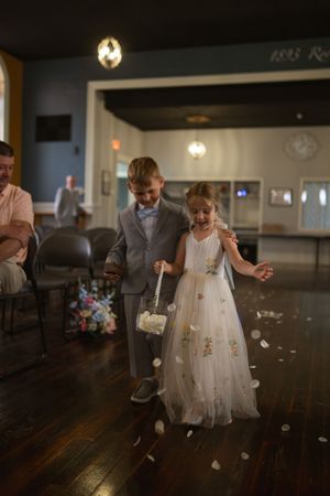 Young attendants in formal wear scatter petals on a dark wooden floor during a wedding celebration.