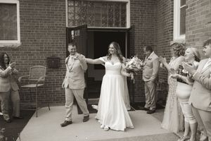 Black and white photo of wedding party gathering outside brick building entrance.