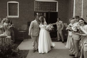 Wedding celebration scene with guests lined against brick wall during outdoor ceremony.