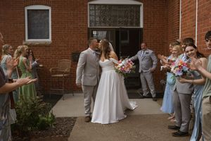 Wedding party gathered outside brick building with bridesmaids in light blue dresses and groomsmen in gray suits.
