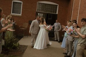 Wedding party and guests mingling outside red brick building during celebration.