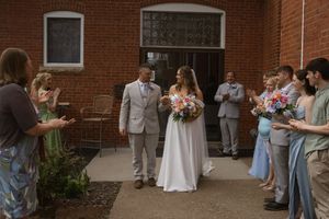 Wedding guests and wedding party lined up against red brick wall during outdoor celebration.