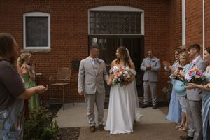 Wedding celebration outside brick building with guests in casual and formal attire.