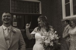 Wedding party members interact outside brick building during celebration festivities.