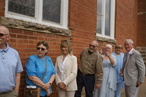 A group of wedding guests gathered outside a brick building on a sunny day.