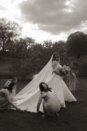 Dramatic black and white photo of wedding dress being arranged in field under cloudy sky.